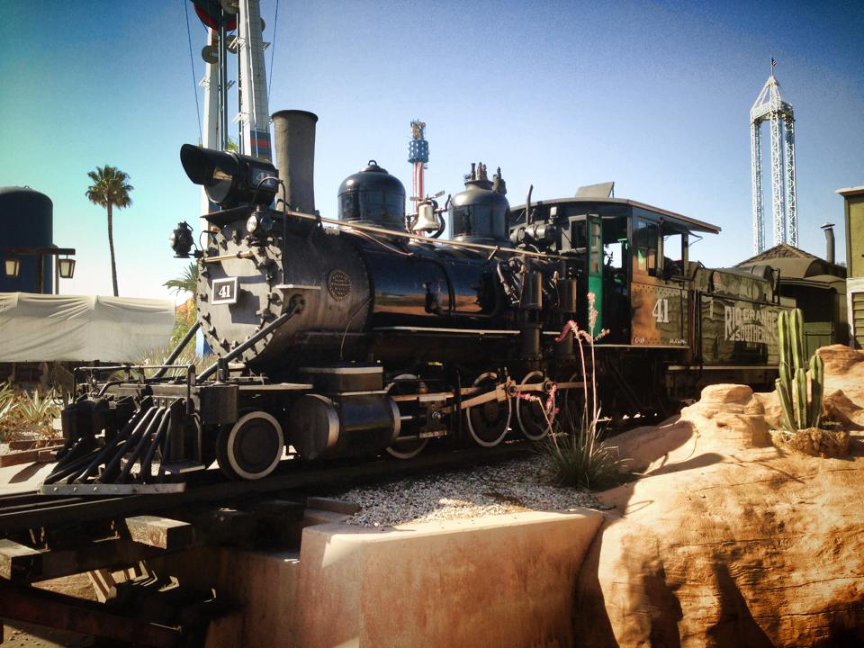 Steam locomotive passes small cactus and themed rock work. 