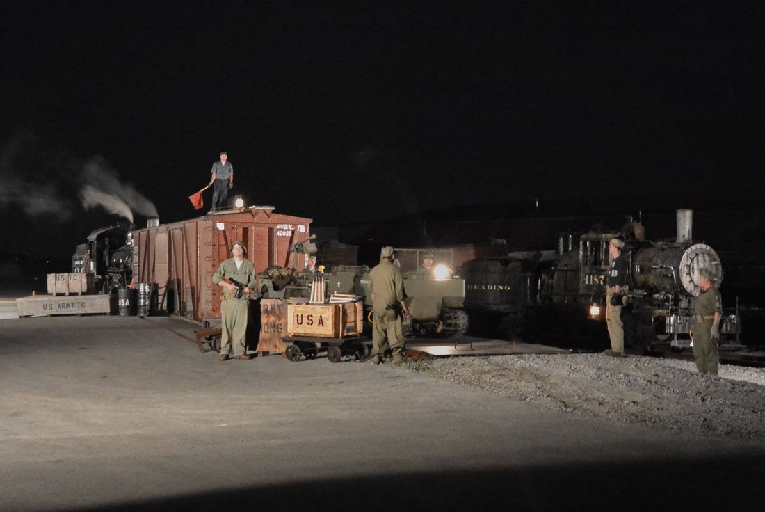 Night Photography with steam locomotives and a box car in a rail yard with WWII era actors posing with US Army props. 