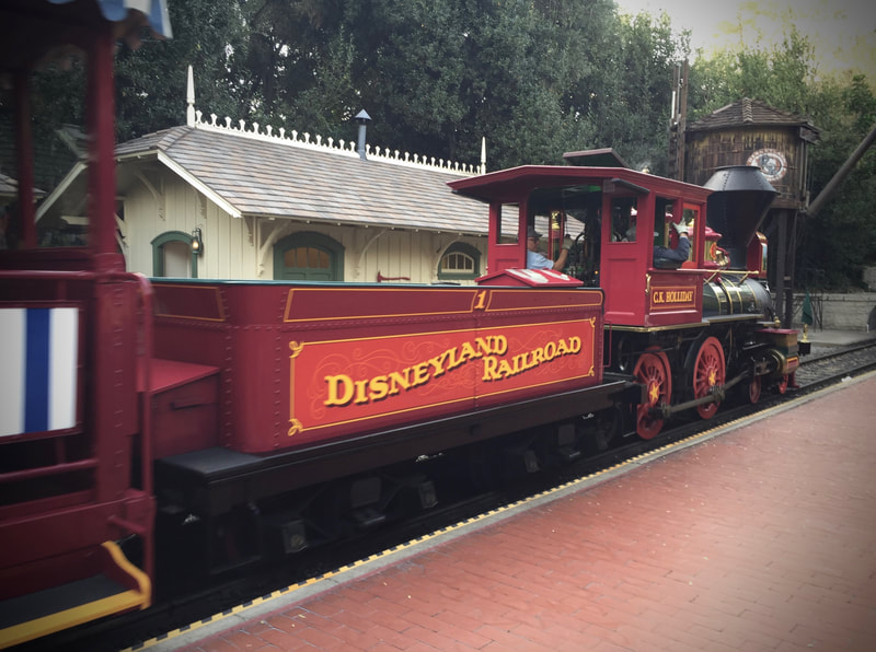 Side view of steam locomotive arriving at station platform. "Disneyland Railroad" written on the tender. 