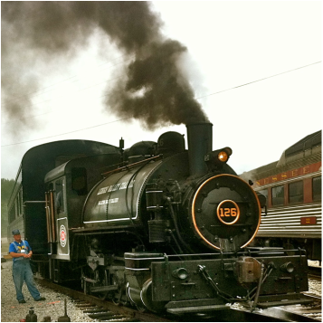 Tank Steam Engine makes smoke, coupled to passenger train. Engineer is standing next to the locomotive. The number 