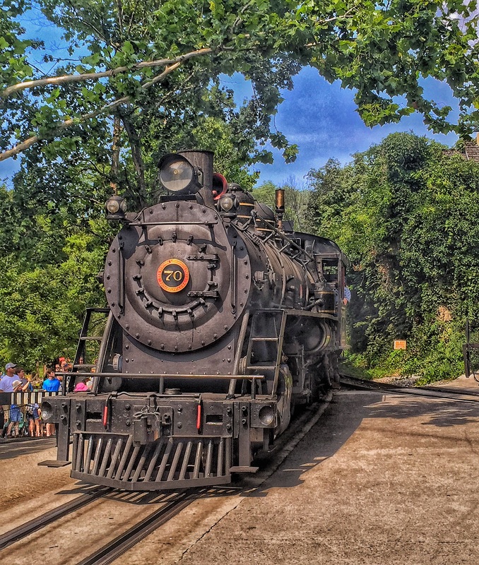 Narrow gauge steam locomotive passes through grade crossing. 