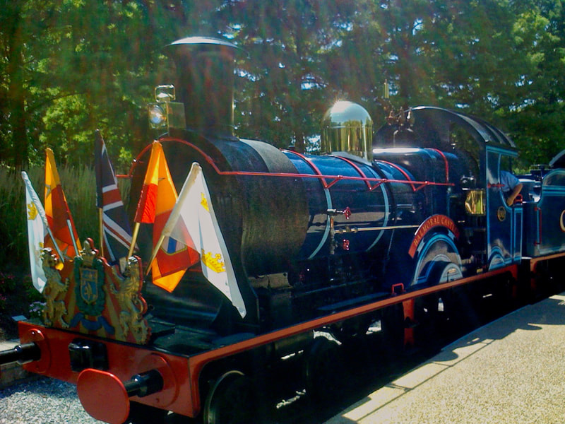 Blue Steam locomotive with British Flags on the front arrives at a train station platform. 