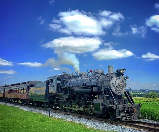 Steam Locomotive pulling a train of maroon coaches through a green field under a blue sky. 
