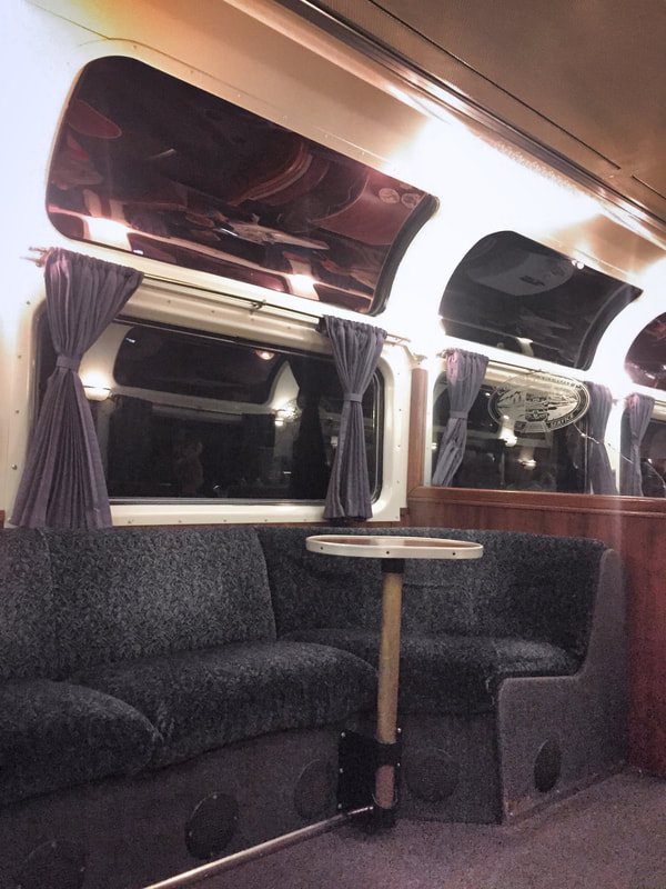 Curved booth, and a small table are n front of double windows inside a Pacific Parlour Car. 
