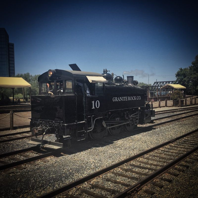 Steam Tank Engine in front of the boardwalk in Sacramento. Photo shows the back of the locomotive where the fuel bunker is. Headlight is above the bunker and lit.