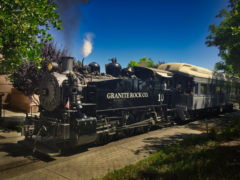 Steam Tank Engine pulls a passenger train. The locomotive says "Granite Rock Co." on the side and the first Train Car is visible behind the locomotive. 
