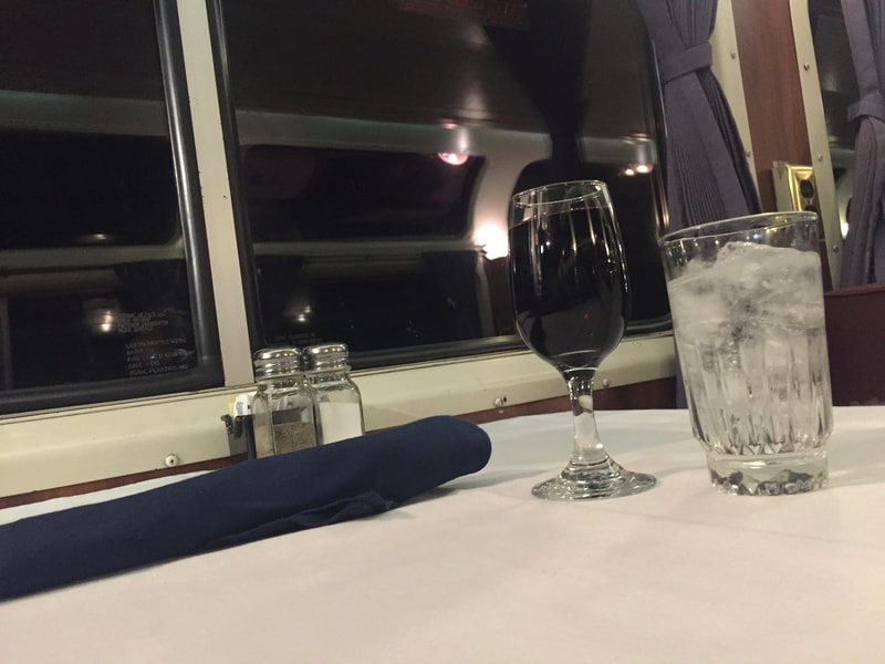 Glass of red wine and glass of ice water on a white table cloth in the Pacific Parlour Car. 