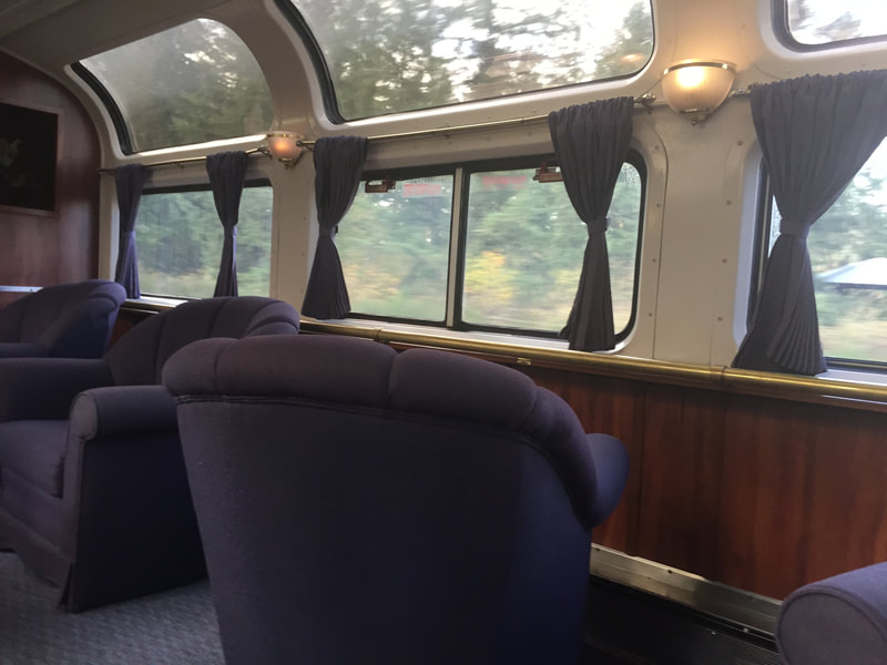 Large, swiveling, purple chairs face the double row of window inside a train car. 