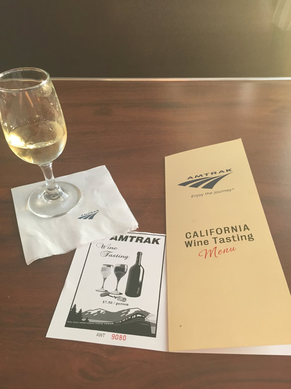 Glass of white Wine on an Amtrak branded napkin next to a menu that reads "California Wine Tasting" 