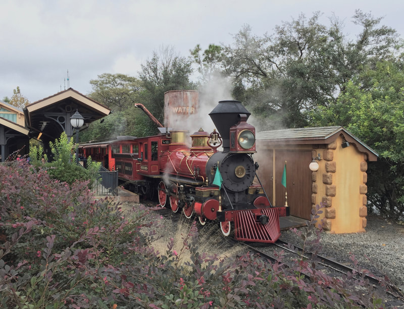 Dark red steam locomotive with green flags lets off steam at station. 