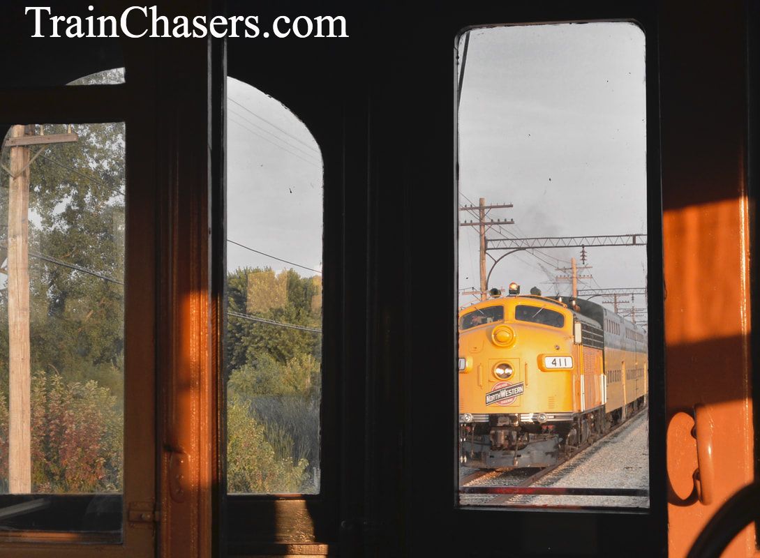 Yellow Diesel Electric Locomotive pulling a bi-level passenger train is seen through the windows of an older electric passenger train. 