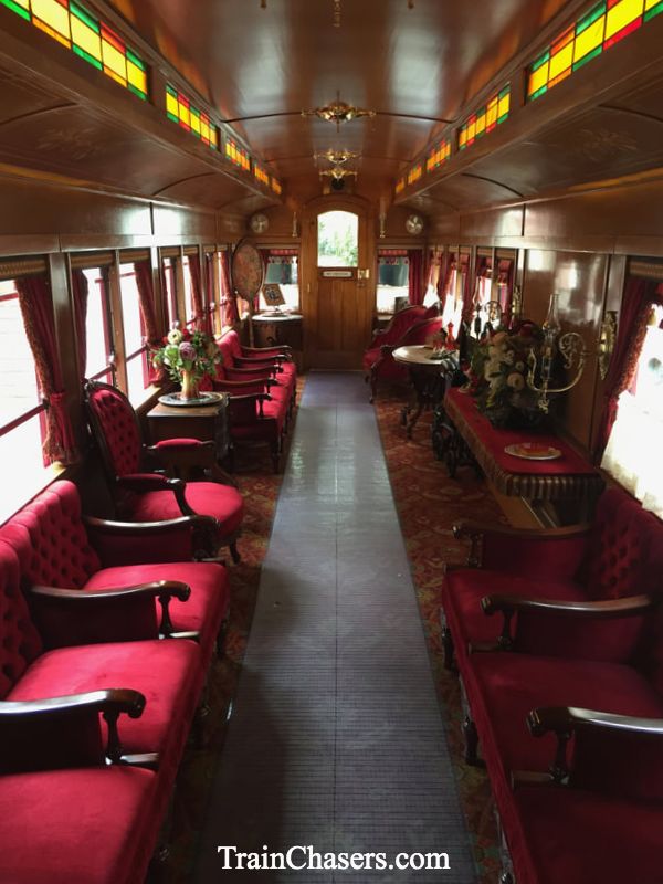 Interior of a train car. Red Plush seats, flowers in vases, and stained glass windows. 