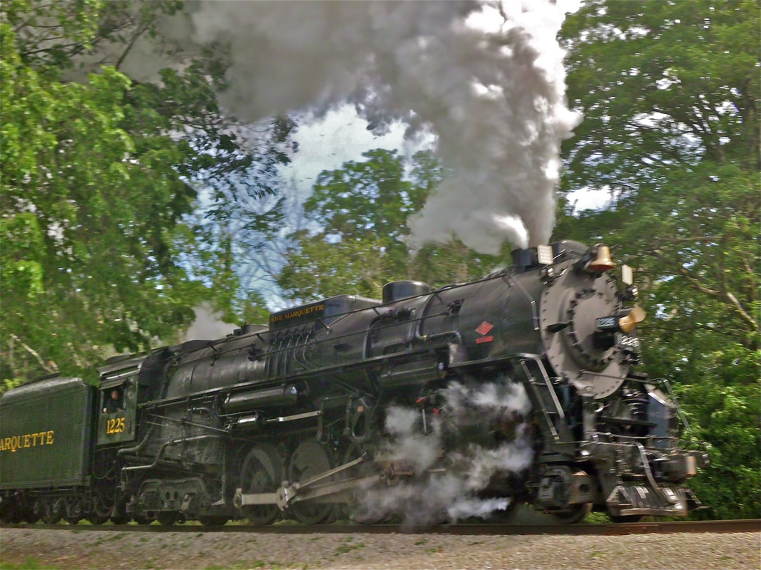 Large Steam Locomotive making smoke and steam as it moves down the track. 